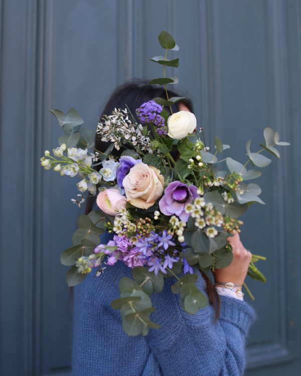 Bouquet de fleurs fraîches dans les tons de violet. Il est composé de : •Rose Equitable •Delphinium •Lisianthus •Wax •Renoncule francaise •Anemone •Genets •Agapanthe •Giroflée •Feuillage